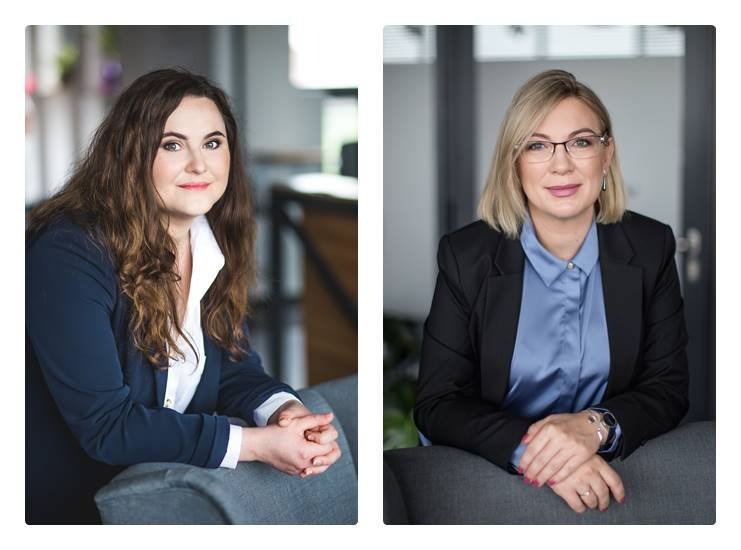 Portret dwóch uśmiechniętych kobiet w biznesowych strojach, opartych o szare fotele w nowoczesnym biurze, prezentujących profesjonalizm i zaufanie.