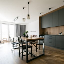 Rem-Rad-Bud Radosław Świętek - Nowoczesna kuchnia z szarymi szafkami, drewnianym blatem i stołem z czarnymi krzesłami. Jasne wnętrze z dużym oknem i roślinami doniczkowymi.