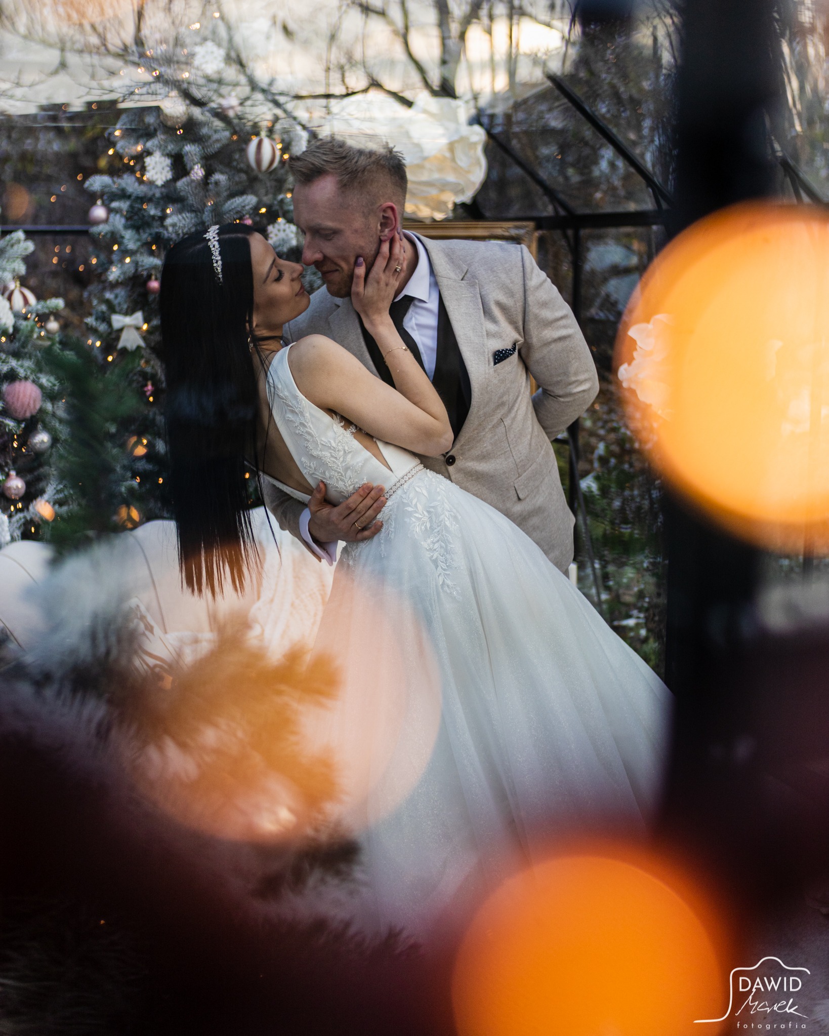 Elegancka para młoda w objęciach na tle świątecznej scenerii z choinką i dekoracjami. Romantyczny moment uchwycony z dbałością o detale i świąteczny nastrój.