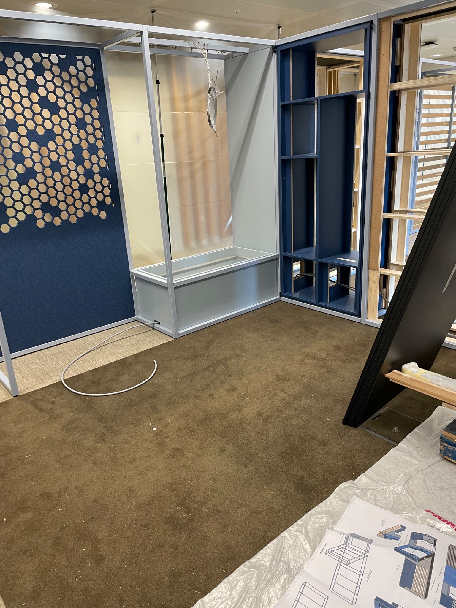 Wnętrze w trakcie wykańczania: zabudowa z płyty karton-gips z dekoracyjnym panelem w geometryczny wzór, widoczne elementy konstrukcyjne i plany techniczne na pierwszym planie.