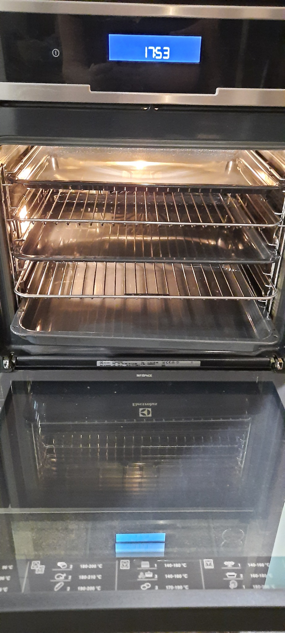 Wnętrze piekarnika Electrolux z wysuwanymi półkami i tackami, widoczne ustawienia temperatury na panelu sterowania. Piekarnik otwarty, gotowy do użycia.