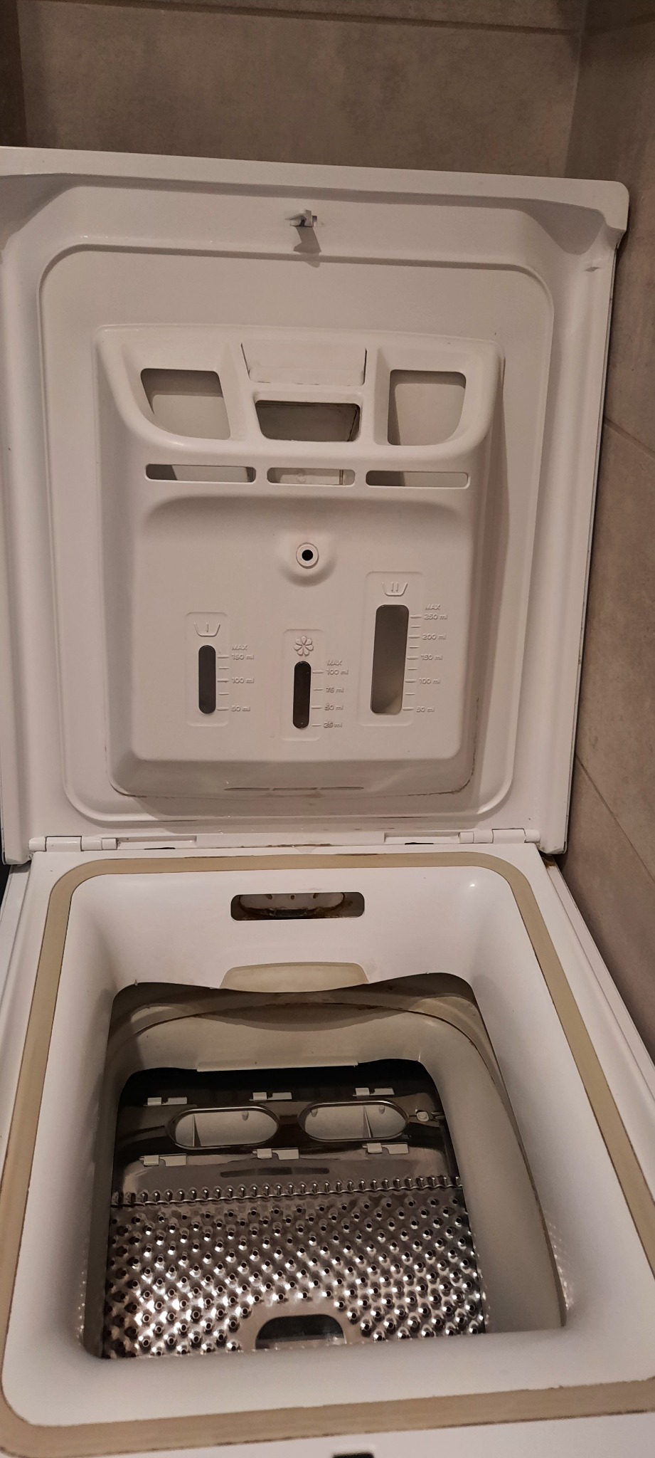 Otwarta pralka z widocznym bębnem i dozownikiem detergentów. Widoczne ślady użytkowania. Ujęcie z góry, skupiające się na wnętrzu urządzenia.