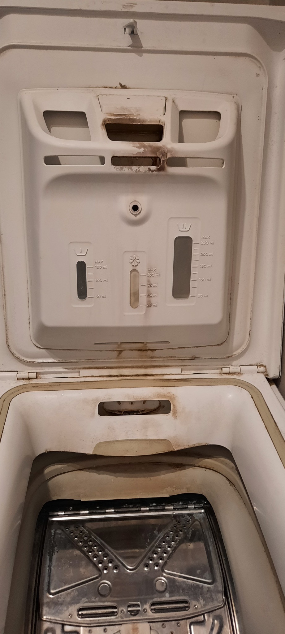 Zanieczyszczona, otwarta pralka automatyczna z widocznymi osadami i zabrudzeniami wewnątrz bębna i na dozowniku detergentów. Potrzeba gruntownego czyszczenia.