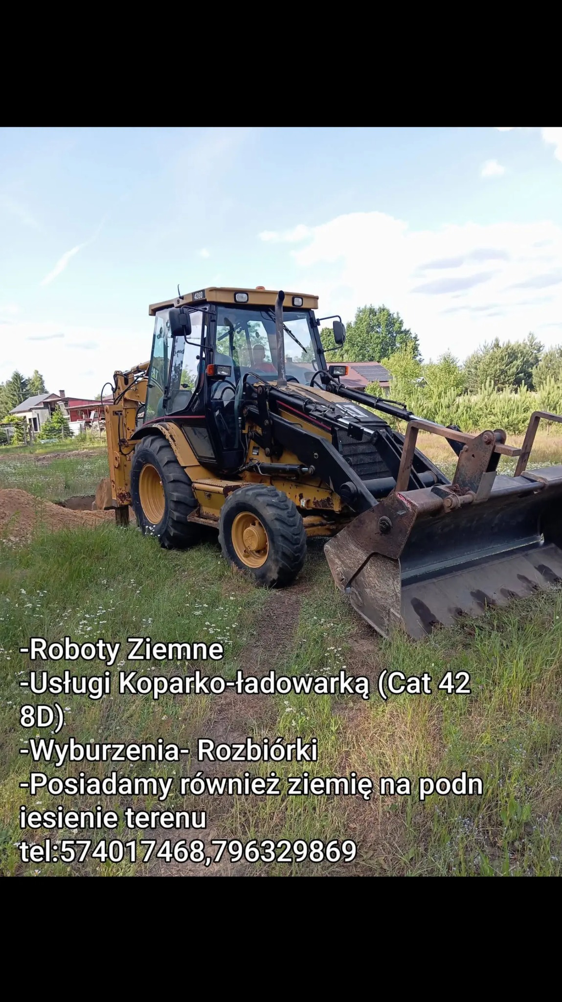 Żółta koparko-ładowarka CAT 428D w trakcie prac ziemnych na działce z zieloną trawą i zabudowaniami w tle. Widoczny wykop. Specyficzne oświetlenie.