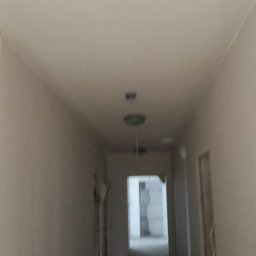 VoltMax - Korytarz w trakcie remontu z zamontowanym oświetleniem sufitowym. Widoczne kable i niedokończone ściany. Ujęcie z dołu, perspektywa w głąb pomieszczenia.