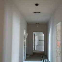 VoltMax - Korytarz w trakcie remontu: świeżo pomalowane ściany, widoczne narzędzia i materiały budowlane, przygotowane do dalszych prac wykończeniowych. Oświetlenie sufitowe.