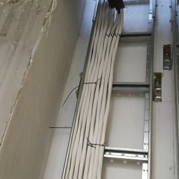 VoltMax - Starannie ułożone białe kable elektryczne na metalowej drabince kablowej, zabezpieczone czarnymi opaskami zaciskowymi, widoczne w otworze sufitu lub ściany.