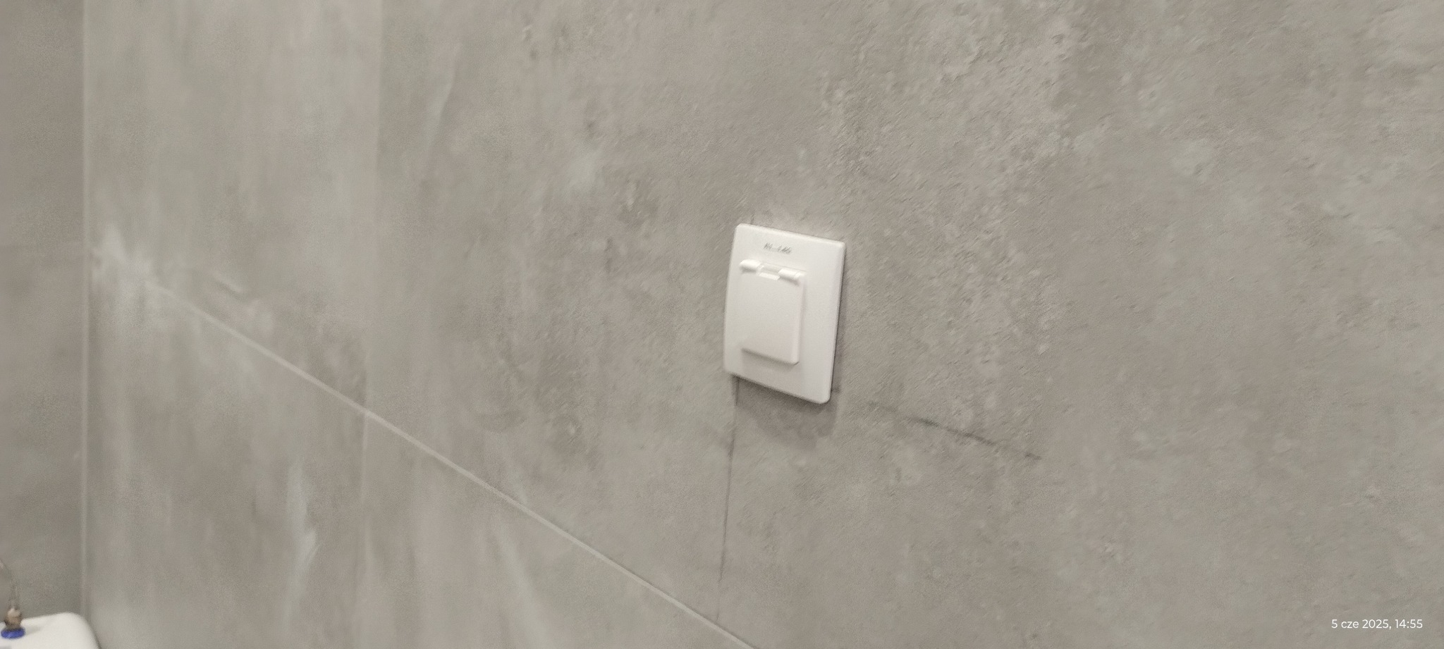 Szary, matowy gres w łazience z zamontowanym białym gniazdkiem elektrycznym. Minimalistyczny design.