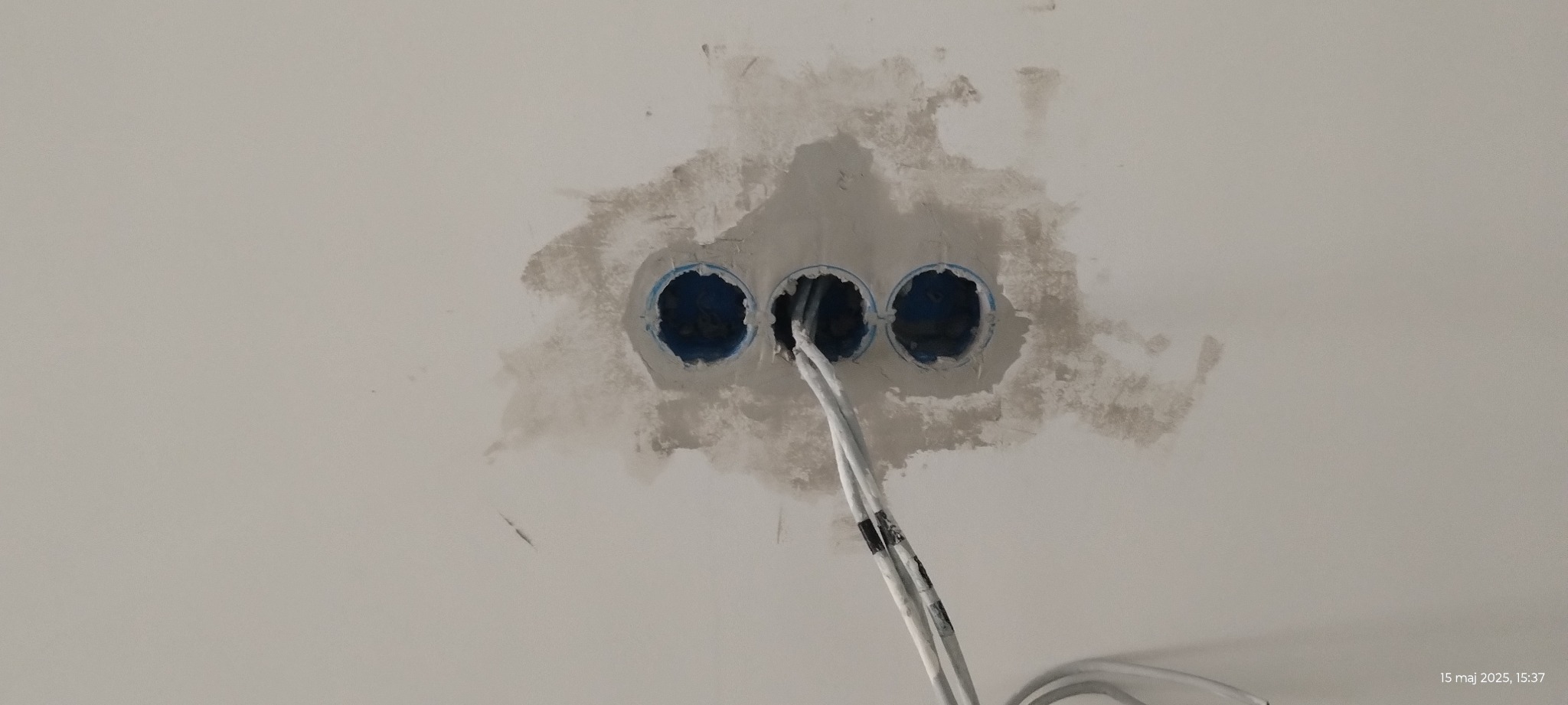 Przygotowane otwory w ścianie z wystającymi kablami elektrycznymi, świeżo po szpachlowaniu, gotowe do dalszych prac instalacyjnych.