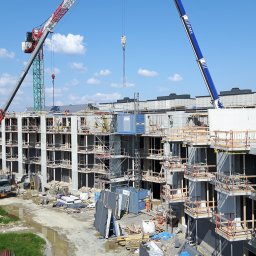 Artur Brzozowski Stombyggen AB - Wielorodzinny blok mieszkalny w budowie w Szczecinie. Widoczne prefabrykaty betonowe, rusztowania i dwa dźwigi. Prace fundamentowe w toku, izolowana płyta betonowa.