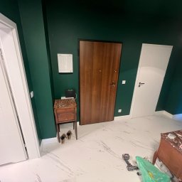 BRUN-BUD - Wykończone wnętrze: biała marmurowa podłoga, butelkowa zieleń ścian, drewniane drzwi i białe drzwi wewnętrzne. Widoczne narzędzia i meble.