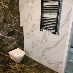 Usługi Remontowo Wykończeniowe BRUN-BUD Karol Kaliniak - Elegancka łazienka po metamorfozie: marmurowe płytki w odcieniach bieli i czerni, wisząca toaleta oraz designerski, czarny grzejnik drabinkowy.