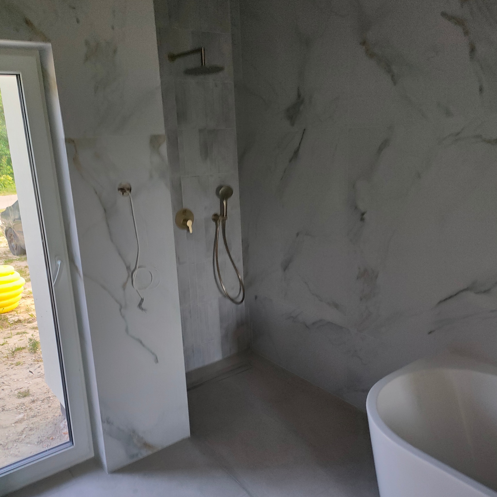 Nowoczesna łazienka w trakcie wykańczania z marmurowymi płytkami, złotą armaturą i widoczną instalacją elektryczną. Fragment wanny owalnej.