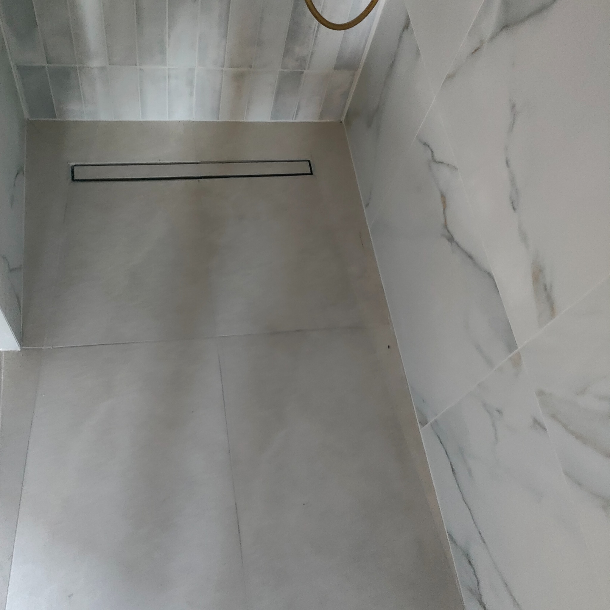 Wykończona łazienka z odpływem liniowym i płytkami imitującymi marmur na ścianie. Ułożone płytki podłogowe w odcieniach szarości. Minimalistyczny design.