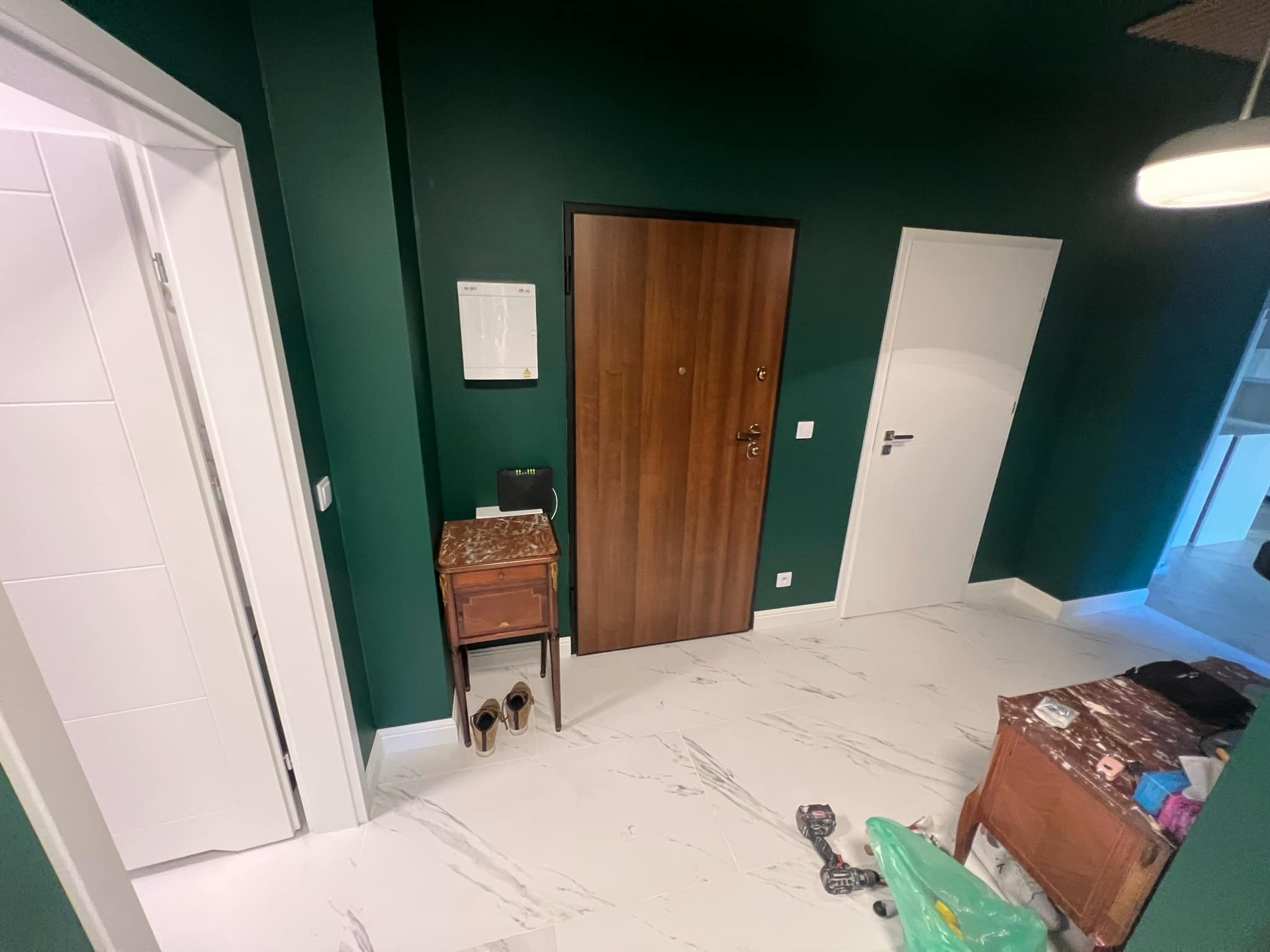 Wykończone wnętrze: biała marmurowa podłoga, butelkowa zieleń ścian, drewniane drzwi i białe drzwi wewnętrzne. Widoczne narzędzia i meble.