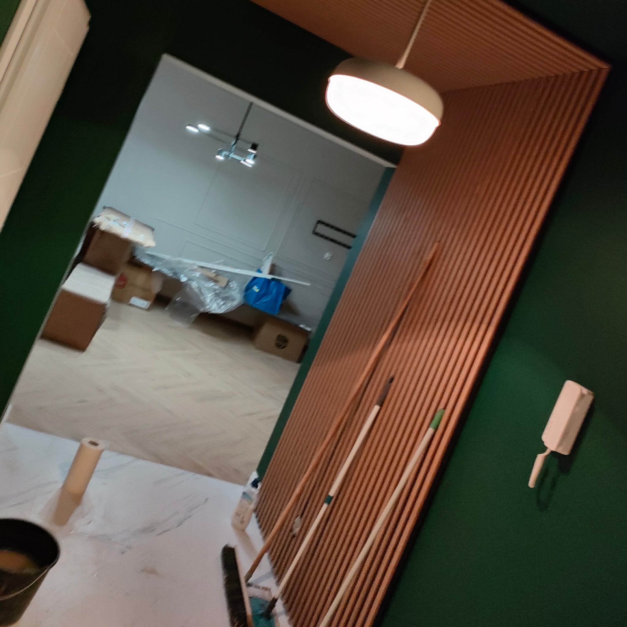 Wnętrze w trakcie prac: widoczne narzędzia malarskie, kartony i wykończona ściana z drewnianymi lamelami. Nowoczesne oświetlenie sufitowe.