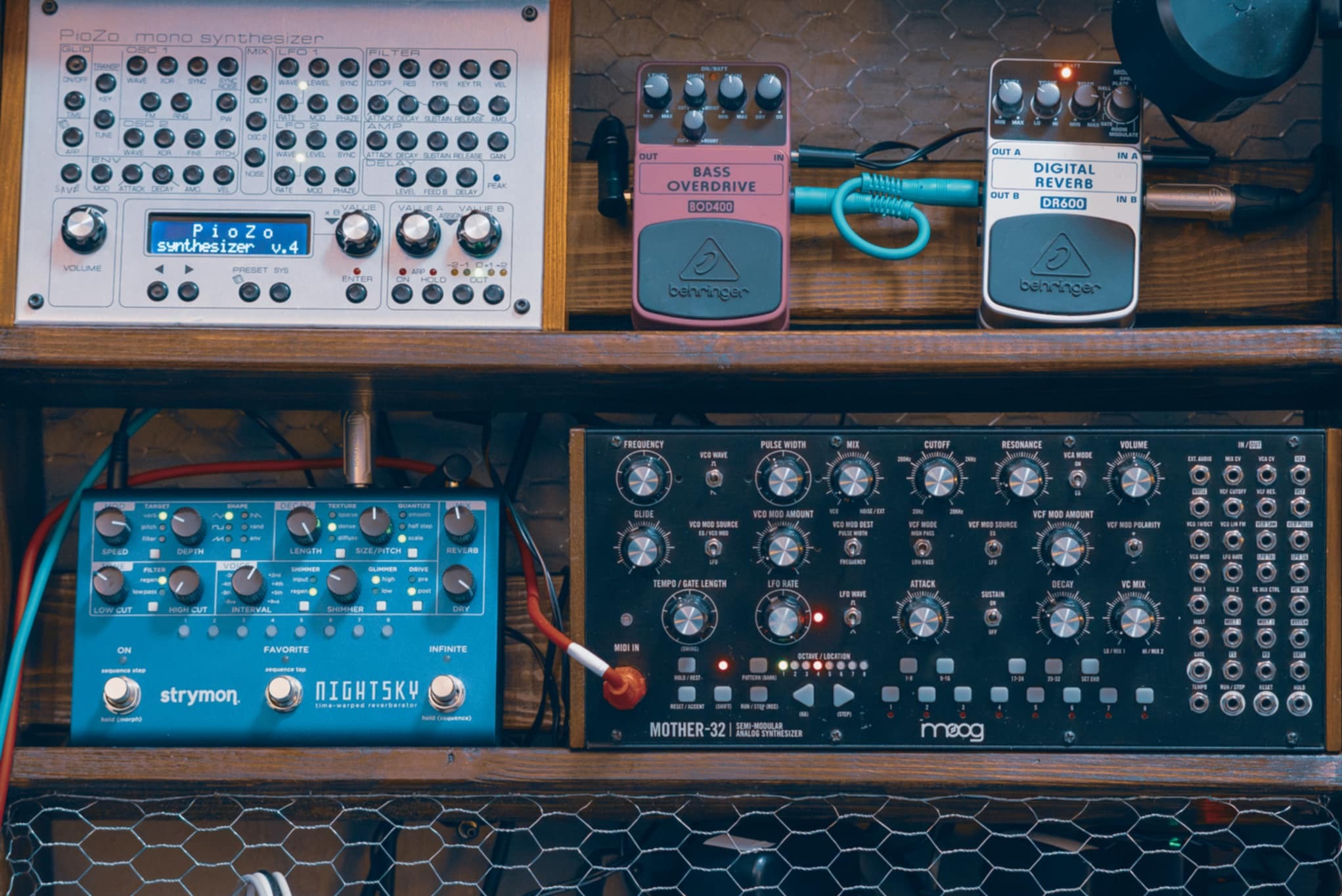 Panel z syntezatorami modułowymi: Moog Mother-32, Strymon NightSky, Behringer BOD400 i DR600, PioZo. Sprzęt studyjny na drewnianym regale z siatką.