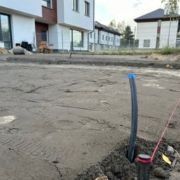 Darek Woźnicki - Przygotowany teren pod trawnik z widocznymi rurami nawadniającymi i wytyczonym obrysem. W tle budynki mieszkalne. Etap prac ziemnych przed założeniem trawnika.