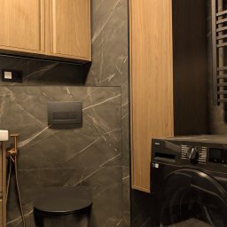 Leonidas & I-BUD - Nowoczesna łazienka z marmurowymi płytkami, wiszącą toaletą i pralką Samsung. Uwagę przykuwają drewniane szafki i złota armatura.