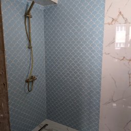 Leonidas & I-BUD - Wykończona łazienka z błękitnymi płytkami w kształcie rybiej łuski i białymi płytkami imitującymi marmur. Widoczny złoty zestaw prysznicowy i odpływ liniowy w podłodze.