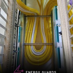 Mateusz Darski ENERGY GUARDS - Uporządkowane kable elektryczne w szafie rack, przewody żółte i białe, ułożone symetrycznie. Widoczne metalowe elementy konstrukcyjne szafy.