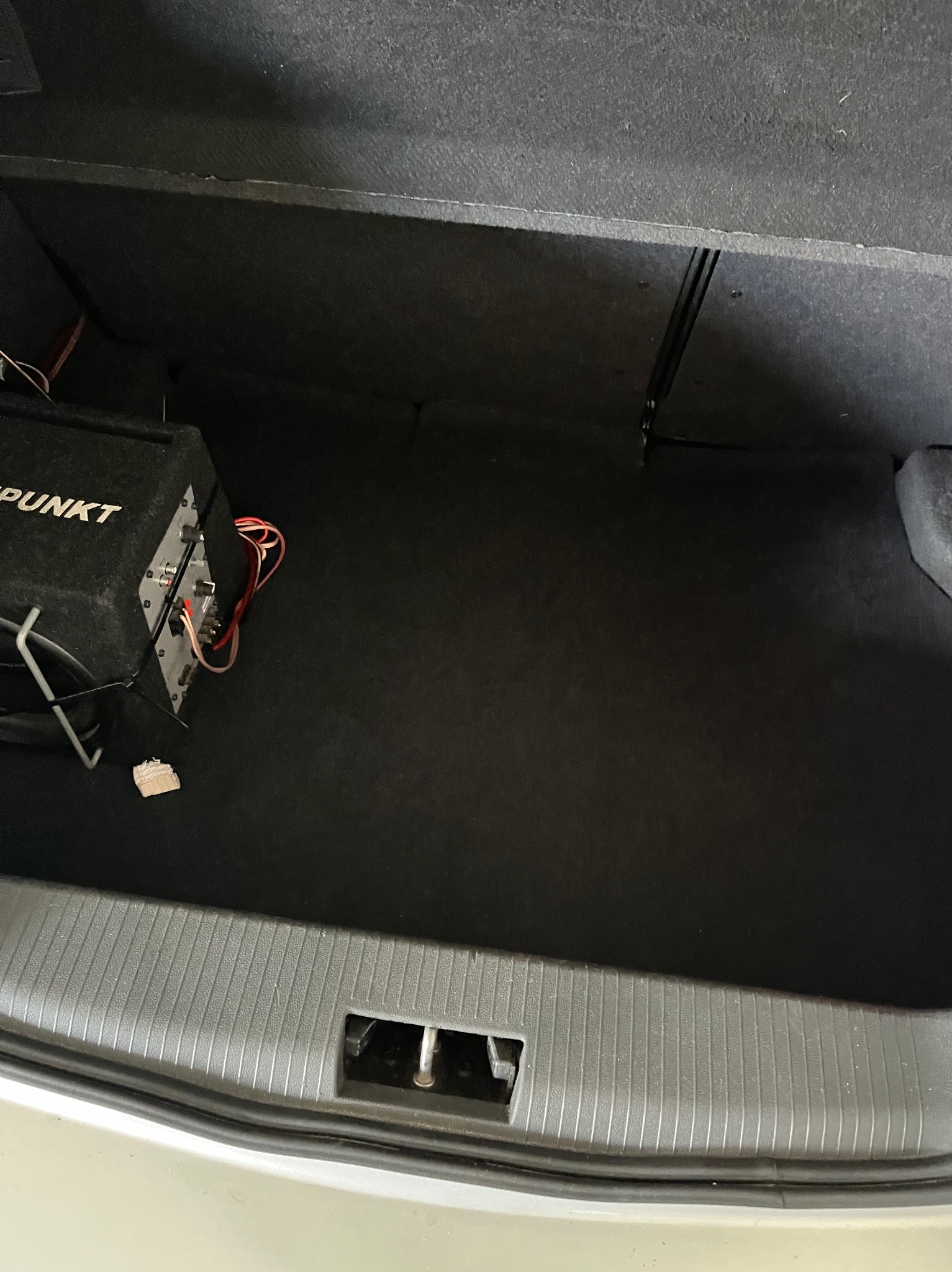 Czarne wnętrze bagażnika samochodowego z widocznym głośnikiem Blaupunkt po lewej stronie i elementami karoserii w dolnej części kadru.