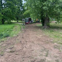 ARBA KAROLINA SŁABIG - Mini koparka na terenie zielonym, przygotowany teren pod prace ziemne. Widoczny sprzęt budowlany i wykopany pas ziemi w otoczeniu drzew.