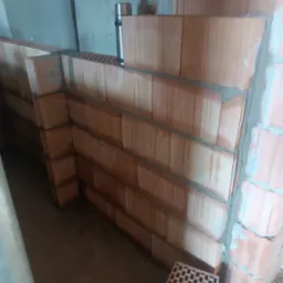 Wznoszenie ściany z pustaków ceramicznych, widoczne spoiny z zaprawy. Na murze stoi termos, a obok leży pojedynczy pustak. Surowe wnętrze w trakcie budowy.