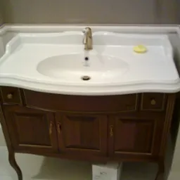 Elegancka szafka umywalkowa z ciemnego drewna i złotej armatury w łazience w Gdańsku. Klasyczny design, biała umywalka z mydłem, subtelne zdobienia.