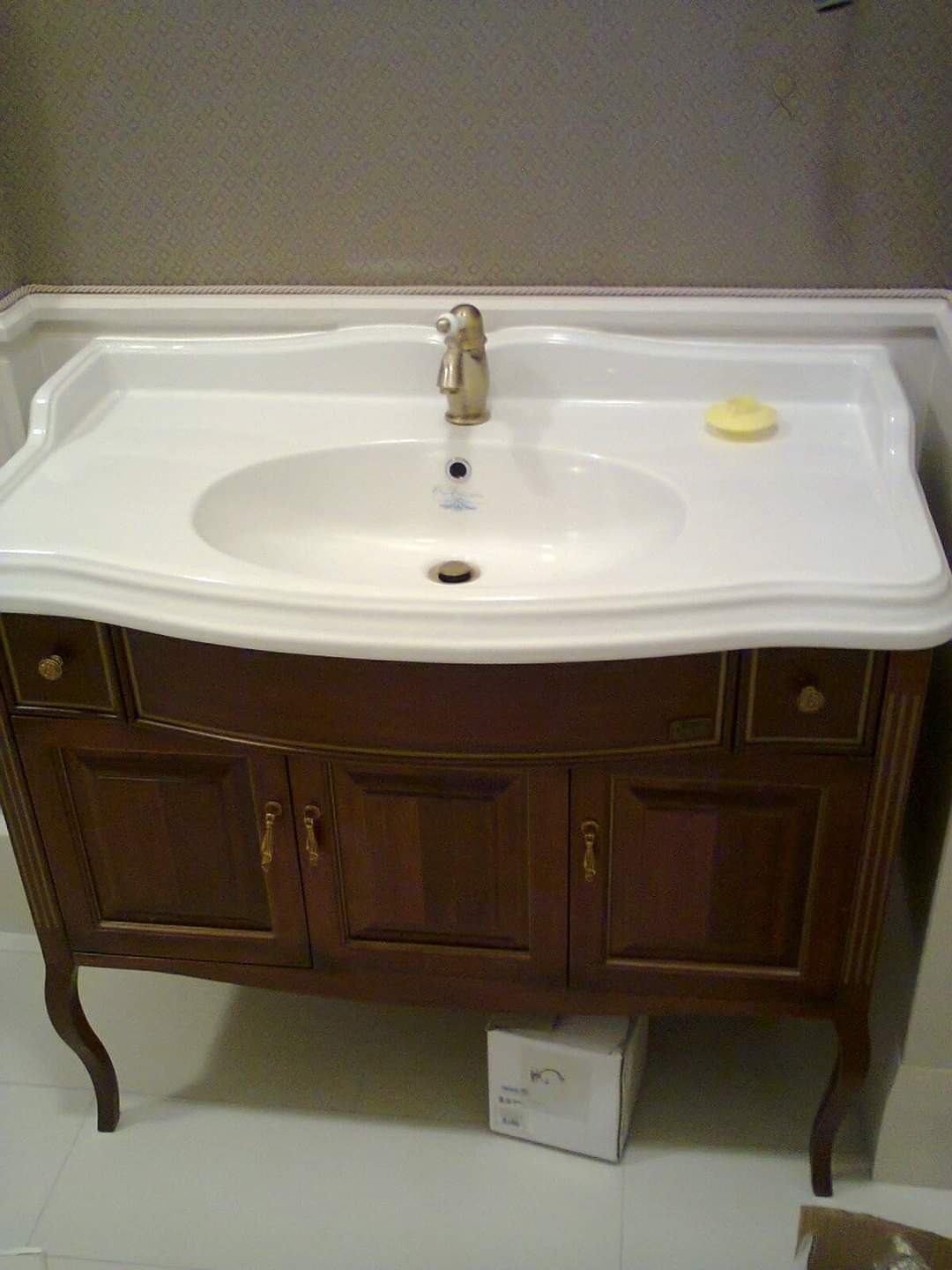 Elegancka szafka umywalkowa z ciemnego drewna i złotej armatury w łazience w Gdańsku. Klasyczny design, biała umywalka z mydłem, subtelne zdobienia.