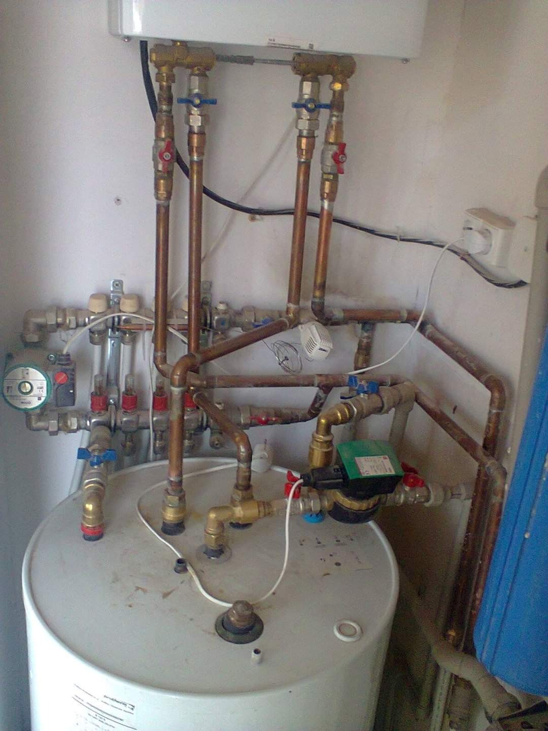 Instalacja grzewcza z piecem i licznymi rurami miedzianymi, zaworami i pompą obiegową. Widoczne przyłącza i elementy sterujące.