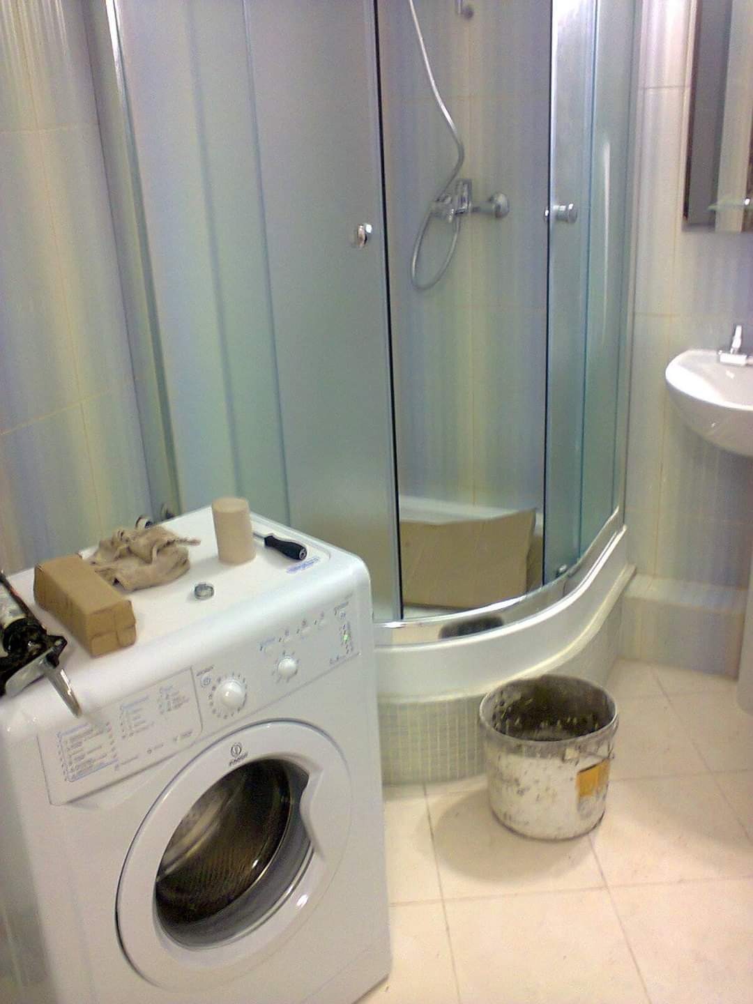 Biała pralka i kabina prysznicowa w łazience z narzędziami na pralce, sugerujące prace hydrauliczne lub instalacyjne w trakcie realizacji.