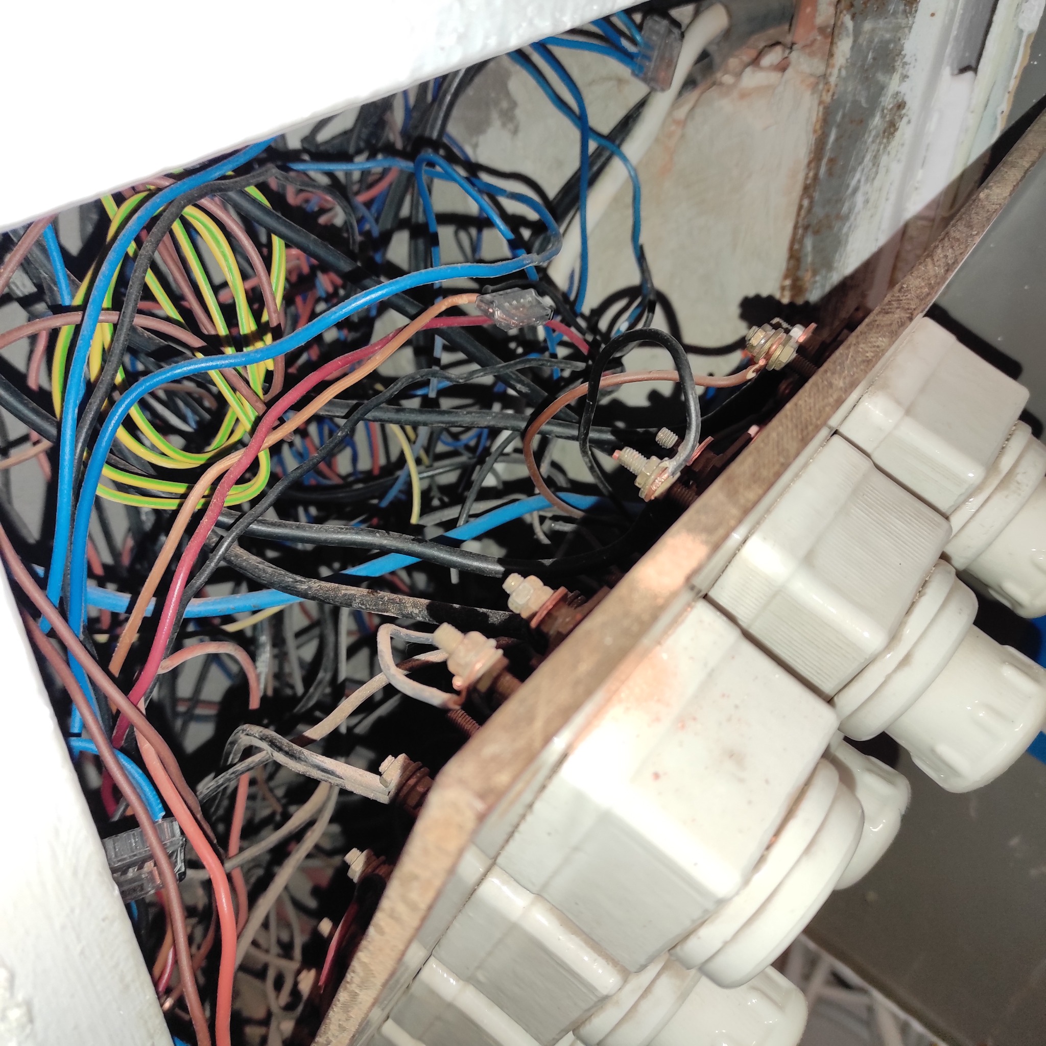 Rozdzielnia elektryczna z widocznymi bezpiecznikami topikowymi i splątanymi przewodami różnej barwy wewnątrz skrzynki, ukazana z bliska.