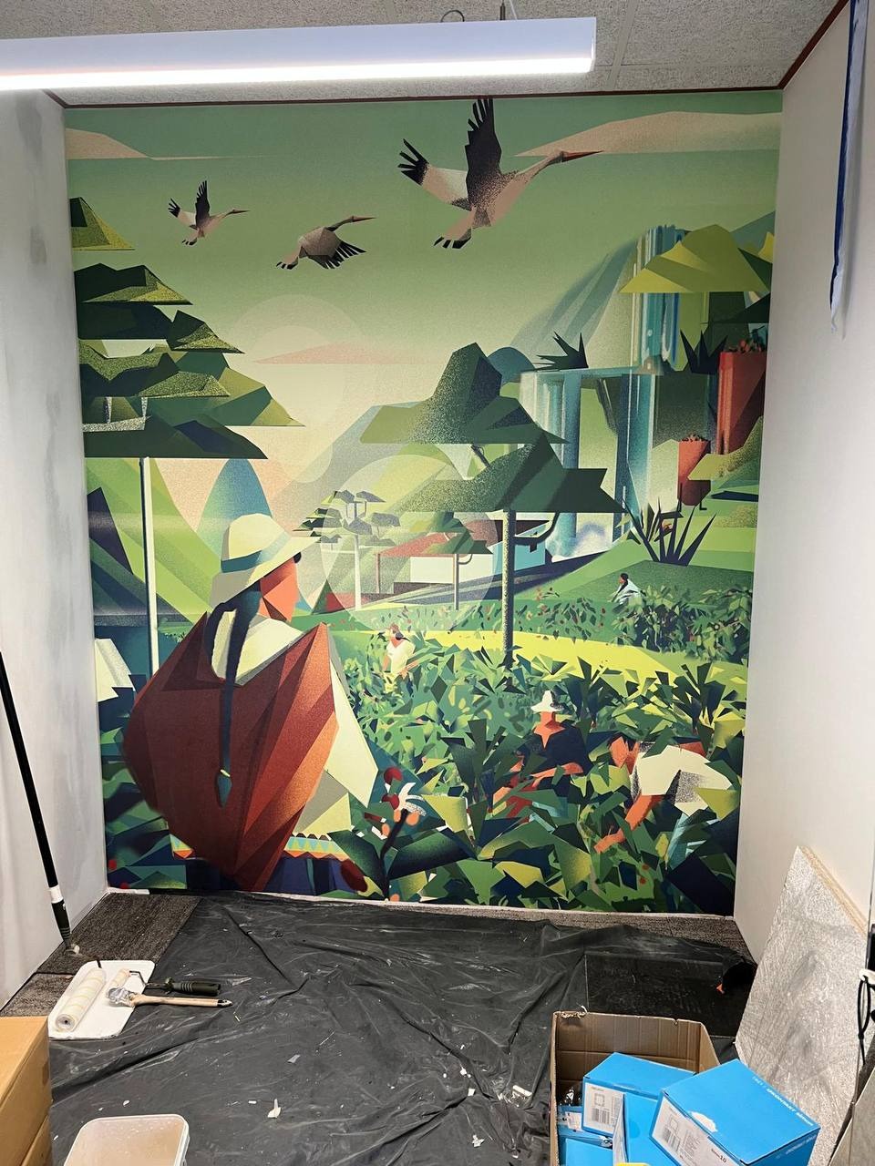 Ściana z fototapetą przedstawiającą krajobraz z motywem ptaków w locie. Na podłodze folia ochronna i akcesoria malarskie, sugerujące świeżo zakończone prace.