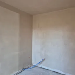 Wnętrze po nałożeniu tynku maszynowego. Widoczne gładkie ściany i sufit oraz fragment instalacji. Dwa otwory w ścianie na instalacje elektryczną.