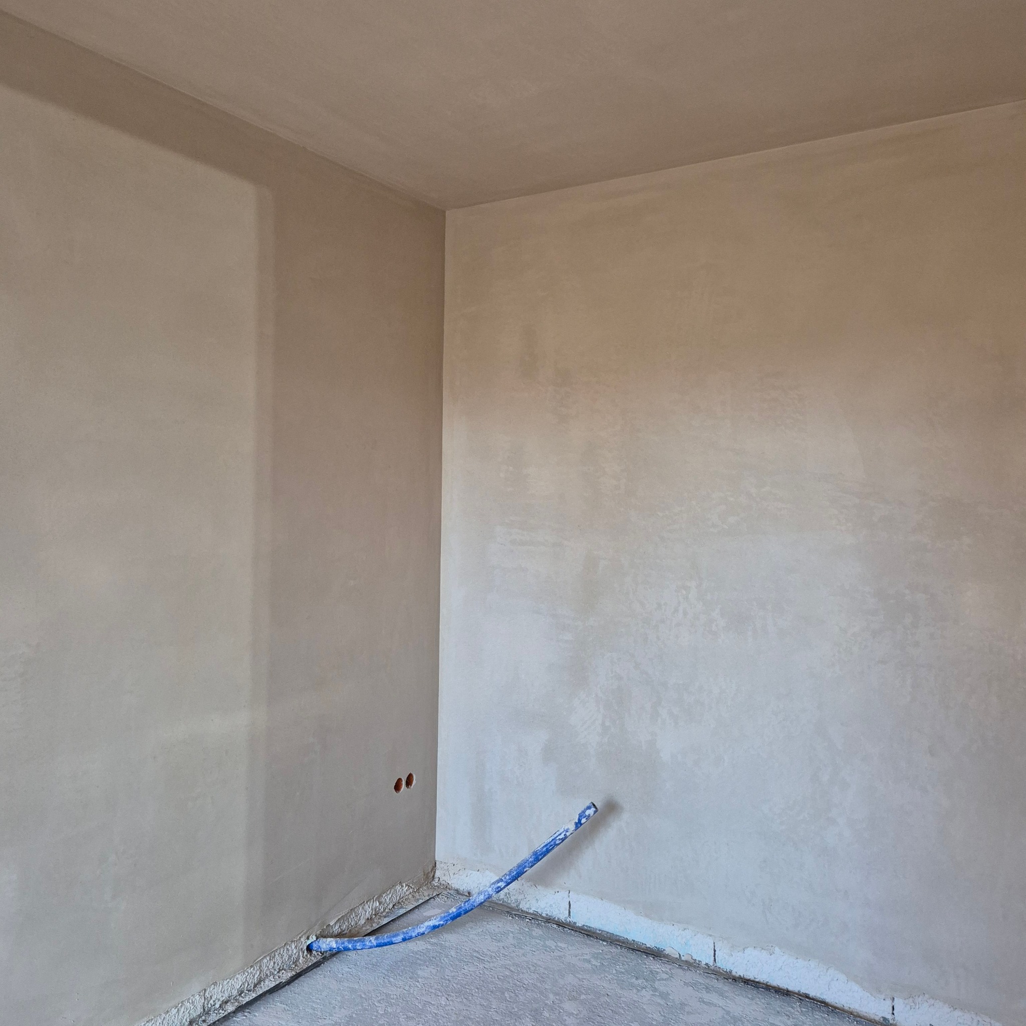 Wnętrze po nałożeniu tynku maszynowego. Widoczne gładkie ściany i sufit oraz fragment instalacji. Dwa otwory w ścianie na instalacje elektryczną.