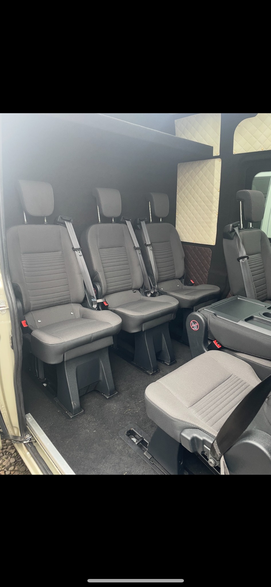 Wnętrze busa z trzema rzędami szarych foteli z pasami bezpieczeństwa, podłoga w kolorze ciemnoszarym, ściany wykończone panelami tapicerowanymi w romby.