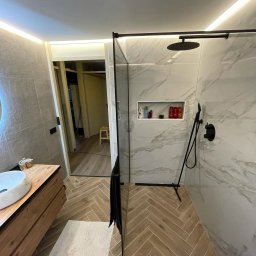MM CONSULTING MACIEJ MAJCHRZYCKI - Nowoczesna łazienka z kabiną typu walk-in, marmurowymi płytkami i drewnianą szafką pod umywalką. Uwagę przykuwa oświetlenie LED i podłoga ułożona w jodełkę.