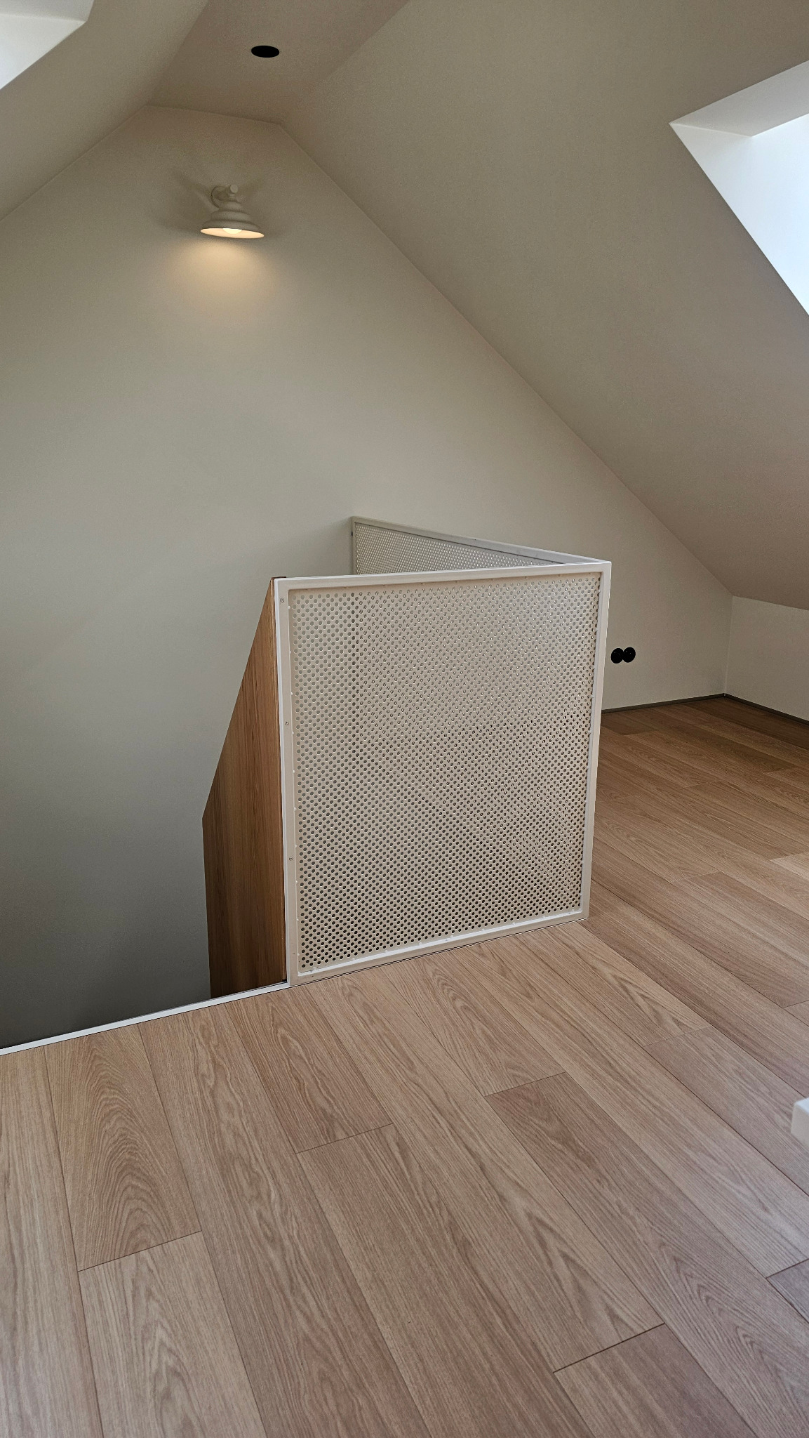 Barierka z siatki perforowanej i profili stalowych, zabezpieczająca schody na poddaszu. Jasne wnętrze, drewnopodobna podłoga, skosy.