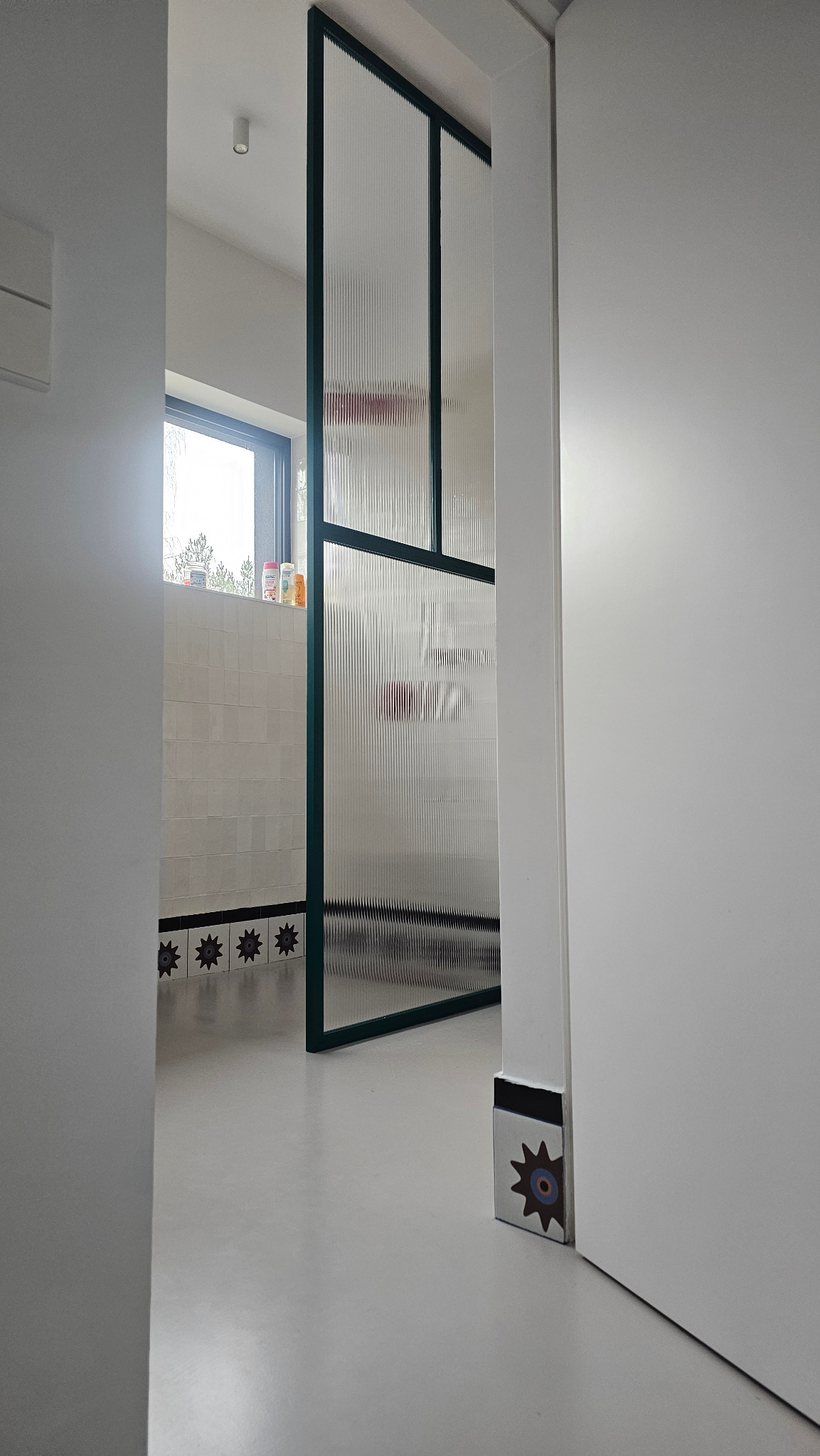 Nowoczesna ścianka prysznicowa z hartowanego szkła flutes i zielonych profili aluminiowych, widoczna z perspektywy wnętrza, z elementami dekoracyjnymi na podłodze.