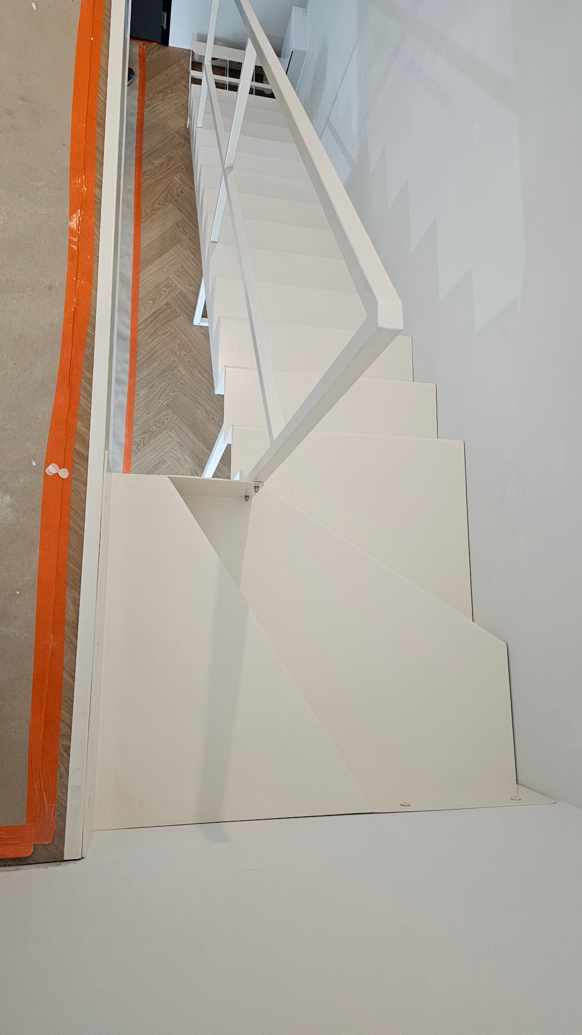 Białe, minimalistyczne schody metalowe z balustradą z profili stalowych, lakierowane proszkowo, widziane z góry, z zabezpieczeniem podłogi w trakcie montażu.