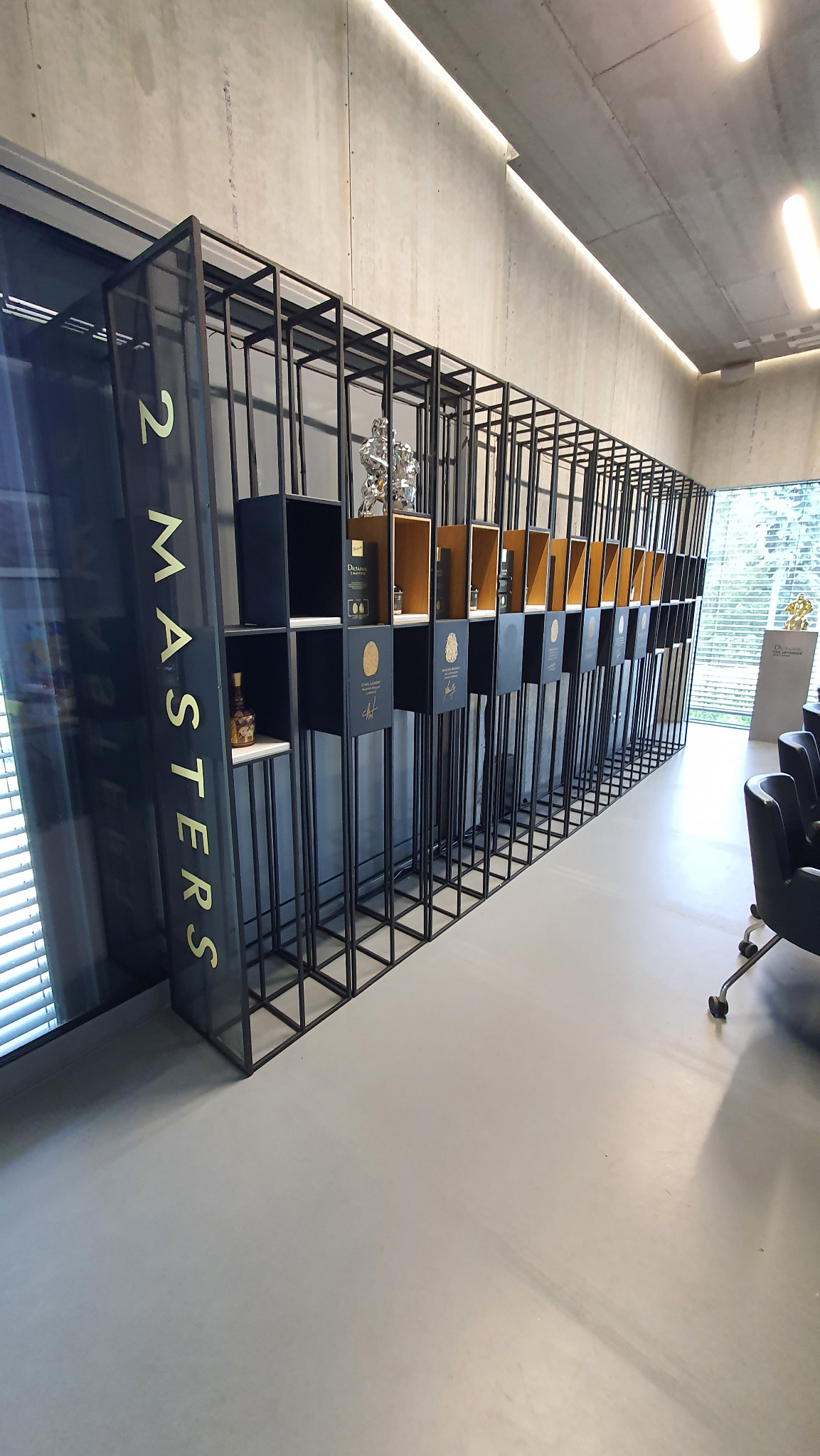 Metalowa, modułowa konstrukcja ekspozycyjna z podświetleniem LED. Czarna rama z półkami prezentującymi produkty. Widok z perspektywy, minimalistyczny design.