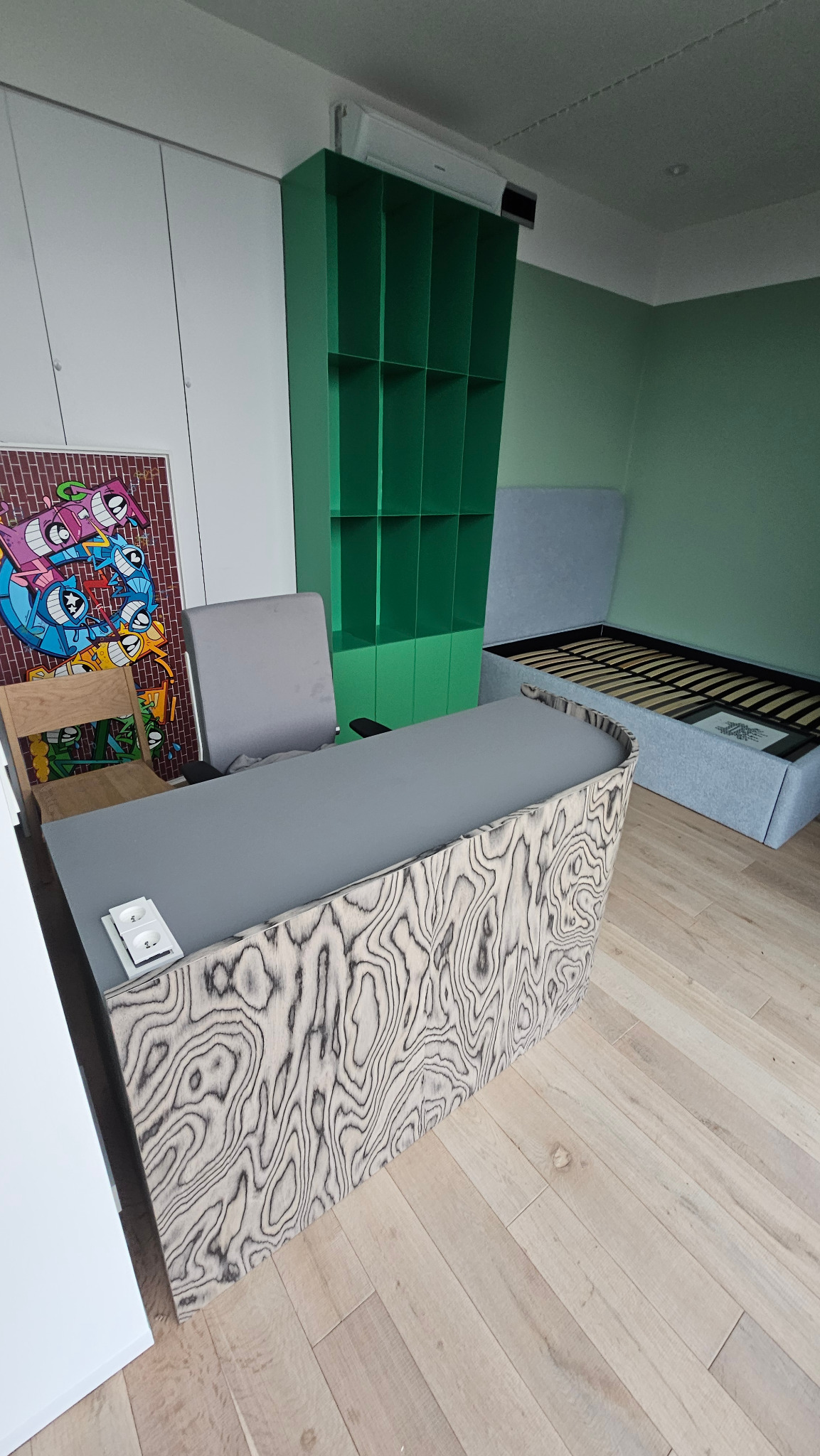 Biurko z forniru i blatem HPL w Gliwicach. Unikalny wzór drewna na froncie biurka. W tle zielona szafka i łóżko z podnoszonym stelażem. Nowoczesny design.