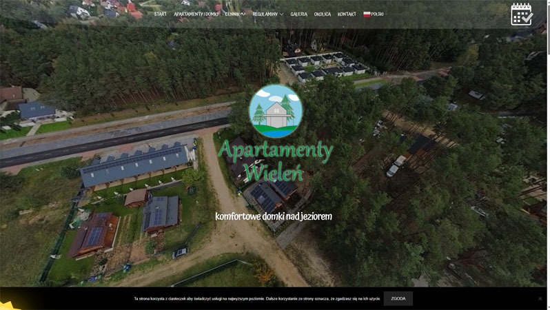 Zrzut ekranu strony internetowej 'Apartamenty Wieleń' z widokiem z lotu ptaka na domki letniskowe otoczone lasem i jeziorem. Logo w centrum, menu u góry, informacja o ciasteczkach na dole.