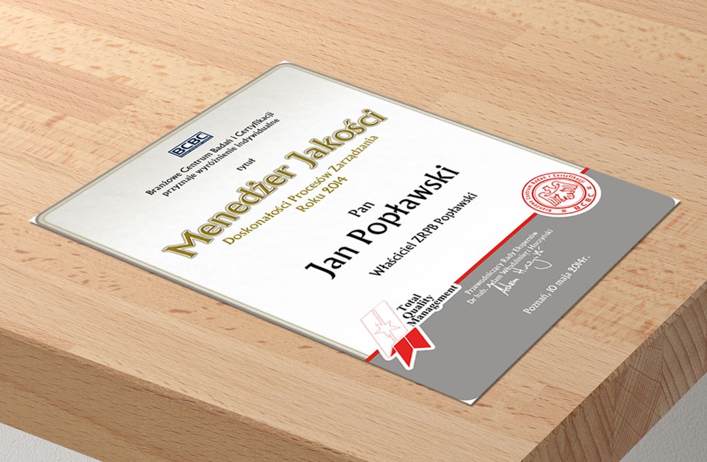 Certyfikat 'Menedżer Jakości' dla Jana Popławskiego z 2014 roku, leżący na drewnianym blacie. Dokument z logo BCBC i podpisami ekspertów.