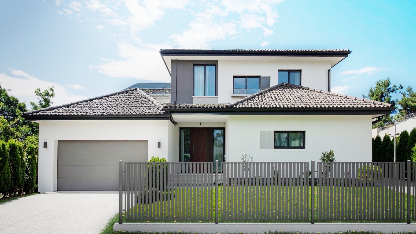 Nowoczesny dom z szarą, pionową, panelową bramą i ogrodzeniem. Minimalistyczna architektura, zielony trawnik, błękitne niebo w tle.
