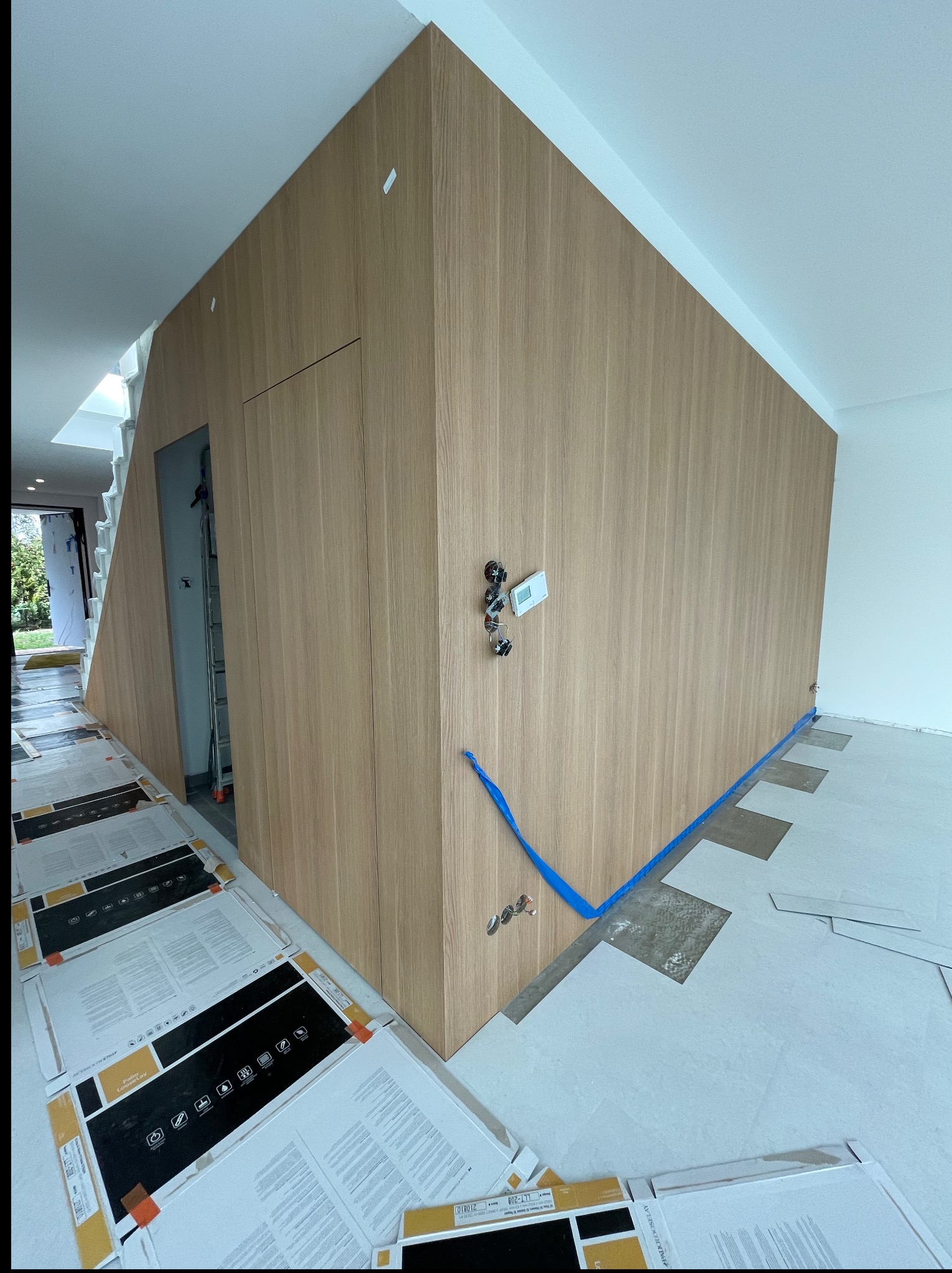 Montaż drewnianej zabudowy wnękowej z ukrytymi drzwiami. Widoczne elementy instalacji elektrycznej i przygotowane panele podłogowe. Surowy stan wykończenia.