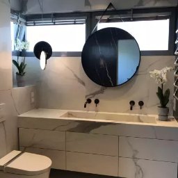 M.K.Bygg Michał Kaczmarski - Nowoczesna łazienka z marmurową zabudową umywalki i okrągłym lustrem. Minimalistyczne czarne baterie i grzejnik w kształcie wieszaka.