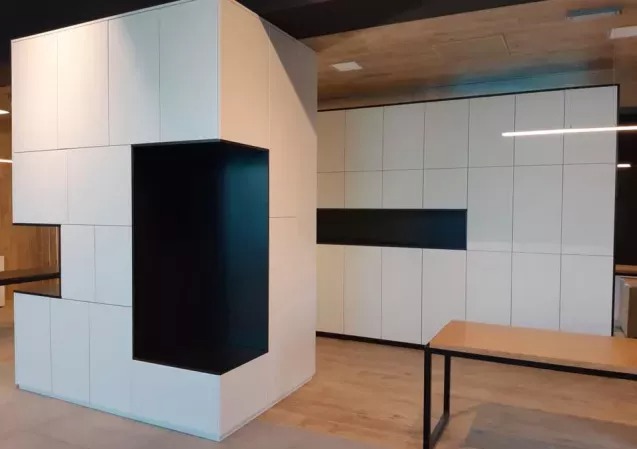 Nowoczesna zabudowa meblowa z białymi szafkami i czarnym, wnękowym elementem, oświetlenie LED, minimalistyczny design, widok na ekspozycję meblową.