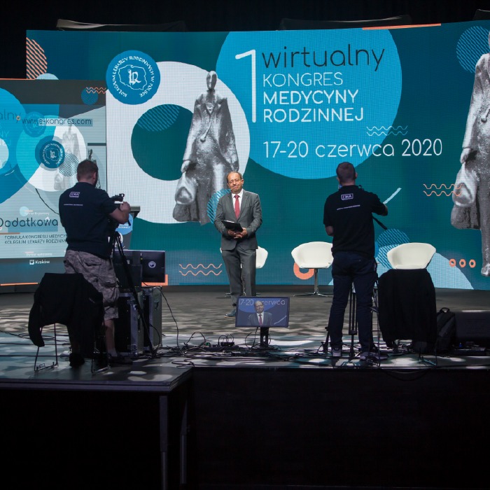 Realizacja wirtualnego kongresu medycznego: prelegent na scenie, ekipa filmowa rejestruje wydarzenie. W tle ekran LED z grafiką i datą wydarzenia.